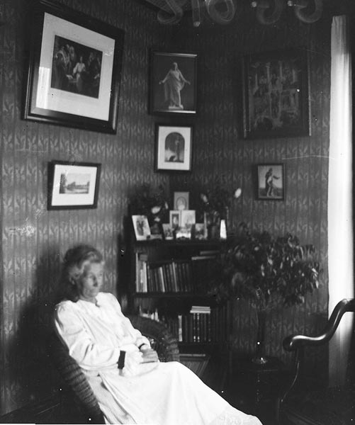 1900 aughts. Ane Koch, my great, great grandmother, sitting in her reading chair. Religious photos adorn the walls.